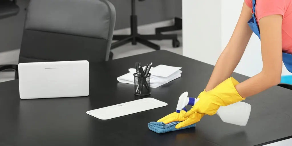 Ein Schreibtisch im Büro wird gereinigt von einem Mitarbeiter der Gebäudereinigung Jäger